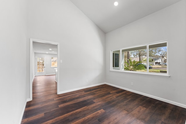 spare room featuring dark wood-type flooring, high vaulted ceiling, and baseboards