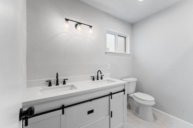 bathroom with toilet, double vanity, a sink, and baseboards