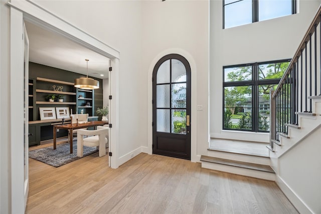 entryway with light wood-type flooring, a high ceiling, stairway, and baseboards