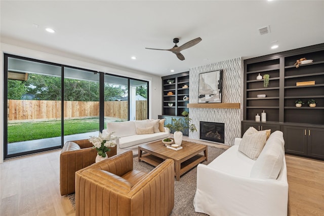 living room with a large fireplace, light wood-style floors, a ceiling fan, and built in shelves