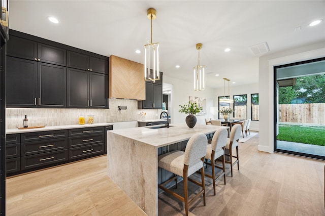 kitchen with tasteful backsplash, dark cabinets, light wood-style floors, a sink, and visible vents