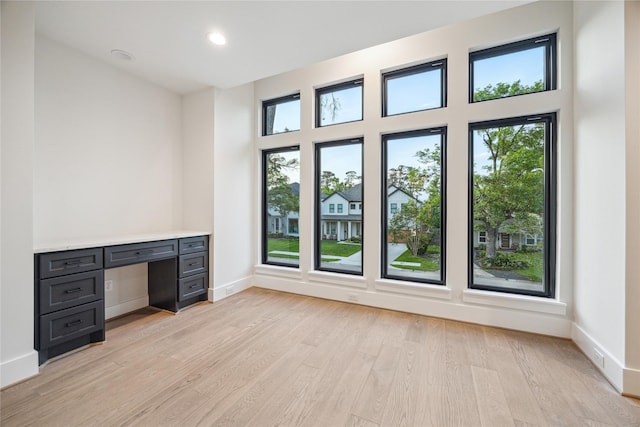 unfurnished office with built in desk, baseboards, light wood finished floors, and recessed lighting