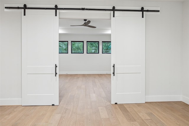 spare room featuring baseboards, a barn door, light wood-type flooring, and ceiling fan