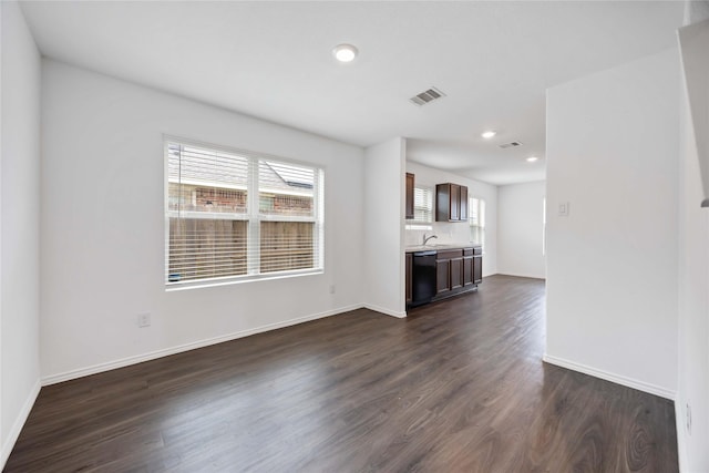 unfurnished living room with visible vents, a sink, baseboards, and dark wood-type flooring