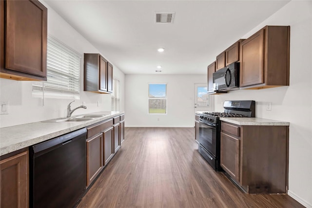 kitchen with visible vents, a sink, black appliances, and dark wood-style floors