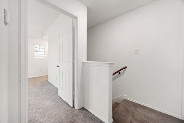 hallway featuring carpet floors, baseboards, and an upstairs landing