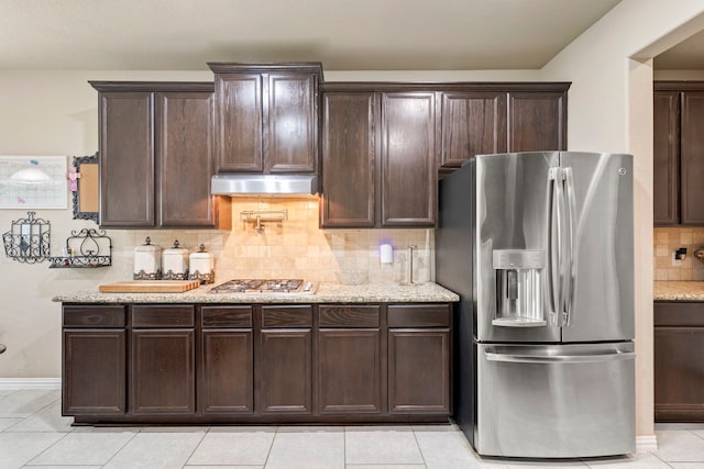 21735 Lozar Dr, Spring, TX 77379 - kitchen with dark brown cabinetry, backsplash, appliances with stainless steel finishes, under cabinet range hood, and light tile patterned flooring