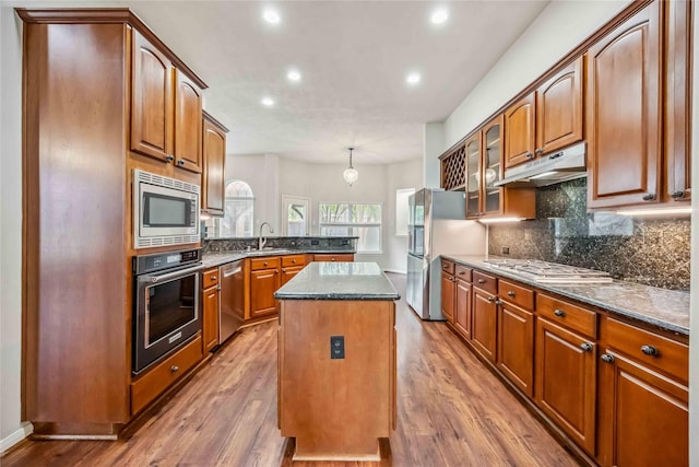 kitchen featuring stainless steel appliances, under cabinet range hood, a sink, a center island, and wood finished floors