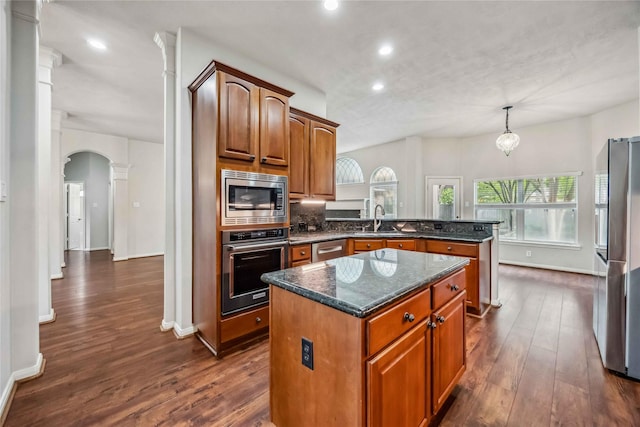 kitchen with stainless steel appliances, a sink, decorative columns, a peninsula, and dark wood finished floors