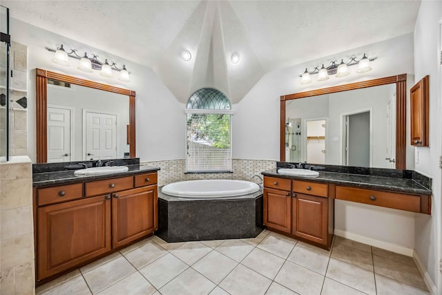 full bath featuring a shower stall, a garden tub, two vanities, tile patterned flooring, and vaulted ceiling
