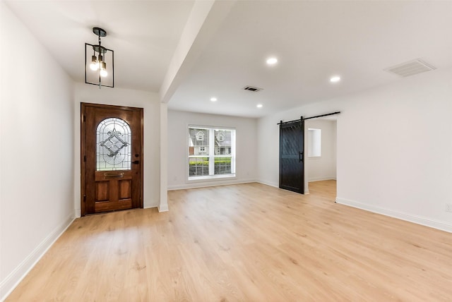 foyer entrance with a barn door, visible vents, light wood finished floors, and baseboards