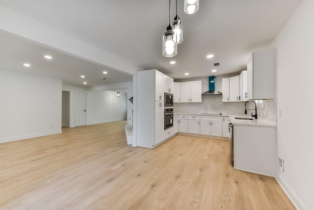 kitchen featuring appliances with stainless steel finishes, light countertops, light wood finished floors, a sink, and wall chimney exhaust hood