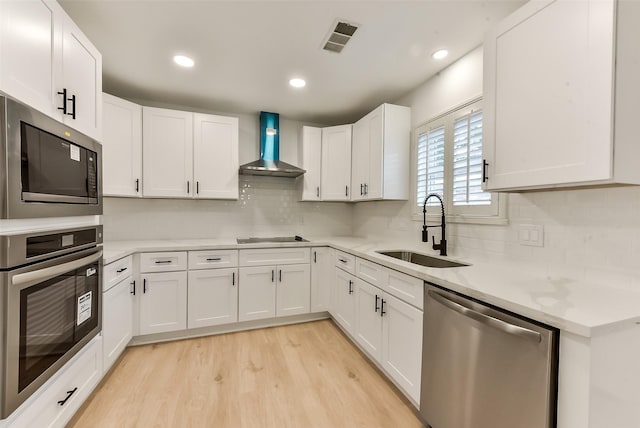 kitchen featuring light wood-style floors, appliances with stainless steel finishes, wall chimney range hood, a sink, and visible vents