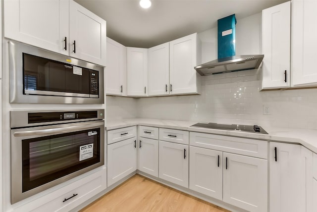 kitchen featuring white cabinetry, light wood-style flooring, stainless steel appliances, light countertops, and wall chimney exhaust hood