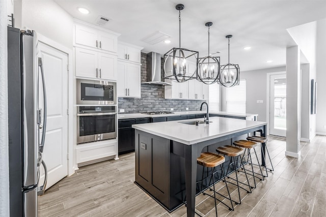4123 Ana Ridge Ln, Fulshear, TX 77441 - kitchen featuring appliances with stainless steel finishes, a sink, wall chimney range hood, light wood-type flooring, and a kitchen island with sink