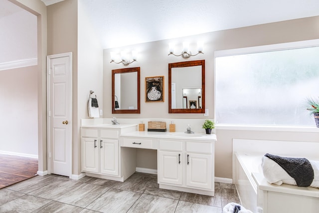 full bath featuring a garden tub, double vanity, a sink, and baseboards