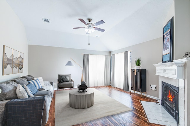 living area featuring wood finished floors, vaulted ceiling, a fireplace, visible vents, and a ceiling fan