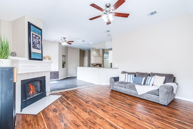 living area with wood finished floors, a tiled fireplace, a ceiling fan, and baseboards