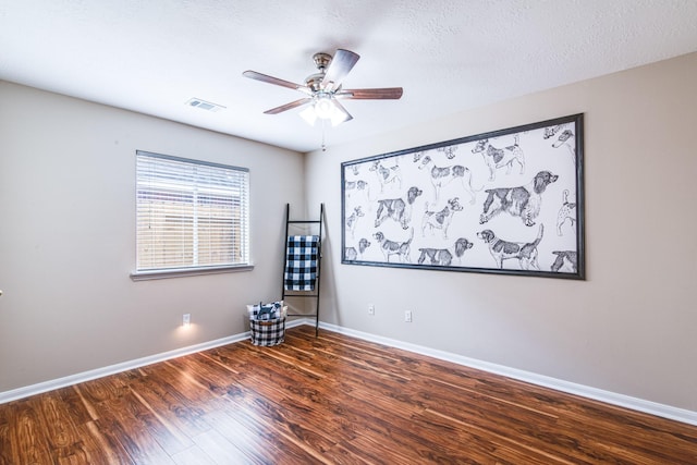 empty room featuring a ceiling fan, visible vents, wood finished floors, and baseboards