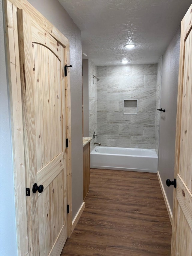 bathroom with baseboards, wood finished floors, a textured ceiling, and tub / shower combination