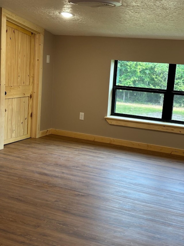 unfurnished room featuring baseboards, wood finished floors, a healthy amount of sunlight, and a textured ceiling