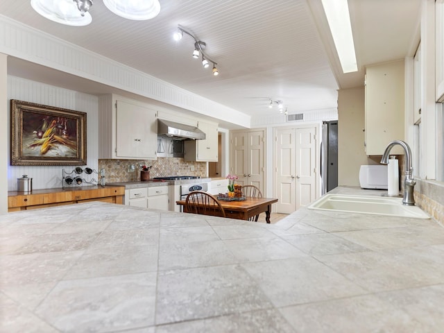 kitchen with a sink, decorative backsplash, wall chimney exhaust hood, track lighting, and visible vents