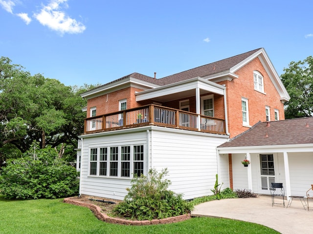 back of house featuring a lawn, a balcony, a patio, and brick siding