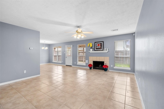 unfurnished living room with ceiling fan with notable chandelier, a fireplace, baseboards, visible vents, and light tile patterned flooring