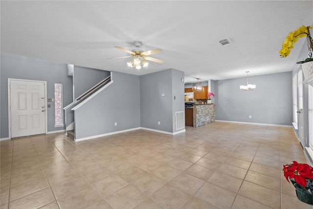 unfurnished living room featuring stairway, light tile patterned floors, visible vents, baseboards, and ceiling fan with notable chandelier