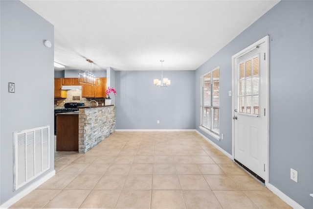 kitchen with an inviting chandelier, hanging light fixtures, brown cabinetry, backsplash, and visible vents