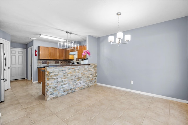 kitchen with light tile patterned floors, brown cabinetry, a chandelier, and decorative backsplash
