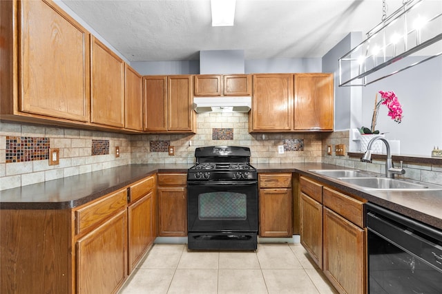 kitchen with black appliances, dark countertops, under cabinet range hood, and a sink