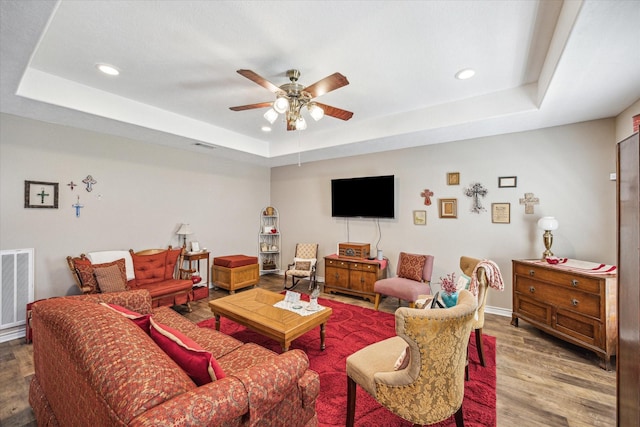 living area featuring a raised ceiling, visible vents, recessed lighting, wood finished floors, and a ceiling fan
