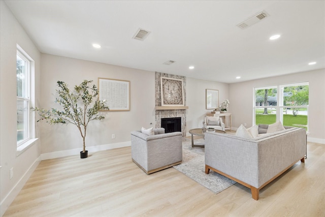 living room featuring light wood-style floors, a large fireplace, baseboards, and visible vents