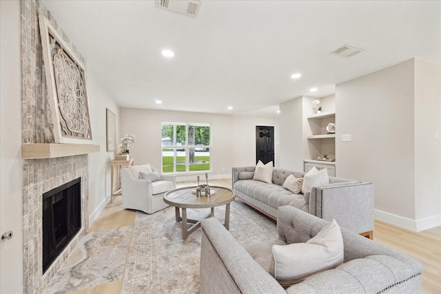 living room with a fireplace, light wood-style flooring, recessed lighting, baseboards, and visible vents