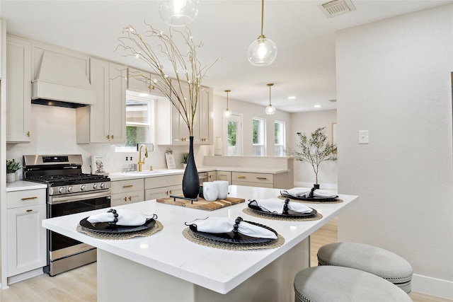 kitchen with visible vents, a kitchen island, premium range hood, light wood-style flooring, and gas stove