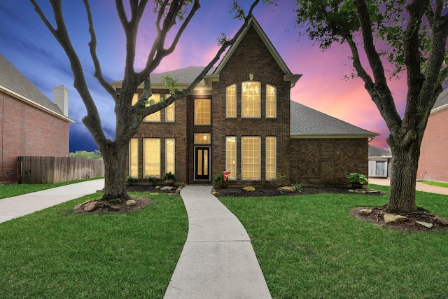 traditional-style house featuring brick siding, fence, a shingled roof, and a front lawn