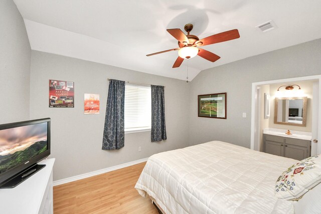 bedroom with visible vents, lofted ceiling, baseboards, light wood-style floors, and ensuite bathroom