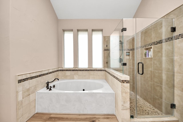 bathroom with a stall shower, lofted ceiling, a bath, and wood finished floors