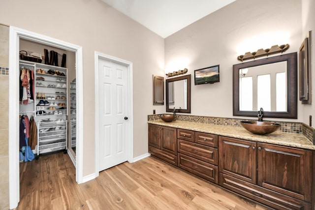 bathroom with a sink, a walk in closet, double vanity, and wood finished floors