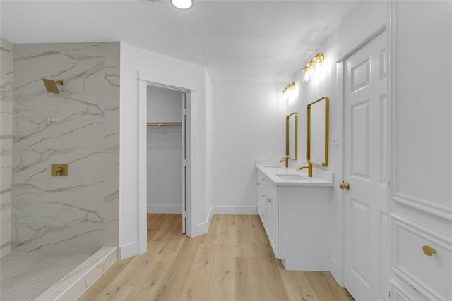 bathroom featuring a spacious closet, wood finished floors, vanity, and a marble finish shower