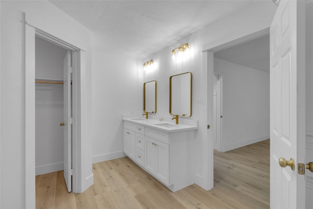 bathroom featuring baseboards, wood finished floors, double vanity, and a sink