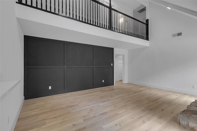 unfurnished living room with baseboards, visible vents, wood finished floors, and a high ceiling