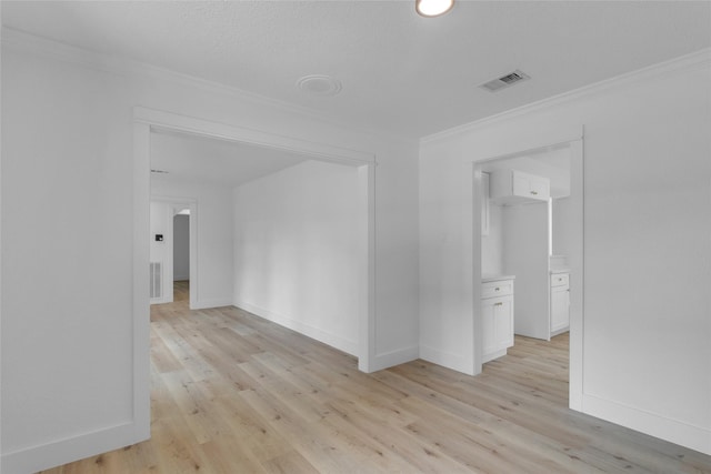 empty room featuring crown molding, visible vents, baseboards, and light wood-style floors