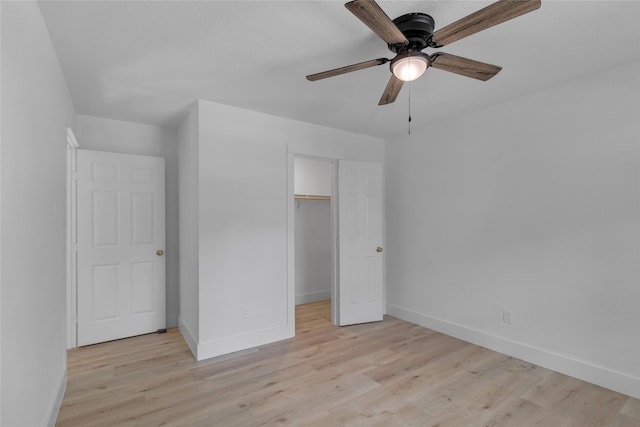 unfurnished bedroom featuring a closet, a walk in closet, baseboards, light wood-type flooring, and a ceiling fan