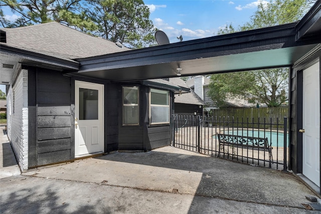 view of exterior entry with fence, a patio area, and a shingled roof