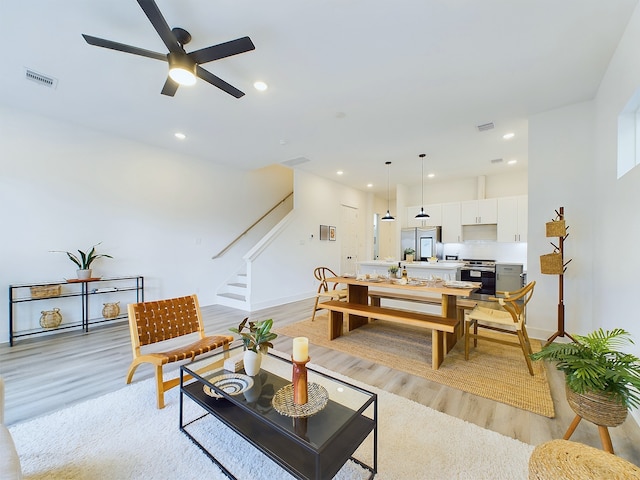 living area with light wood finished floors, stairs, visible vents, a ceiling fan, and baseboards