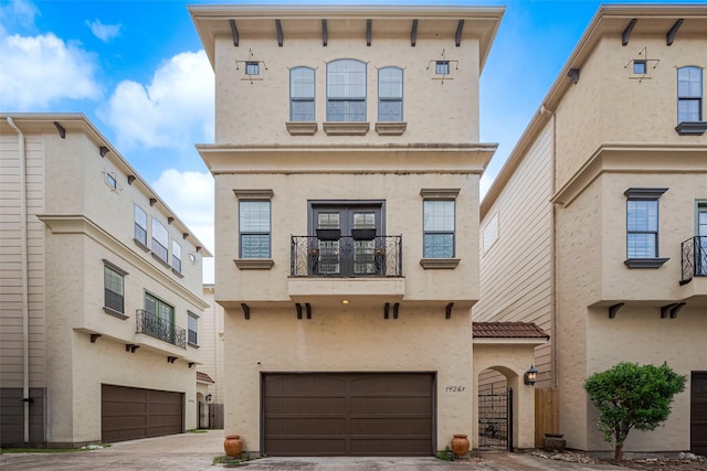 view of front of property featuring a garage, a balcony, a gate, driveway, and stucco siding