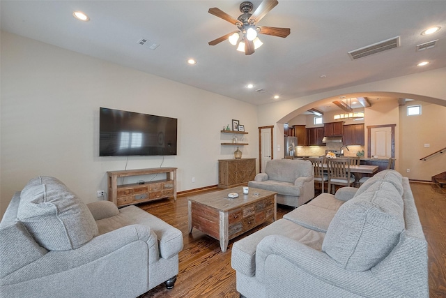 living area with wood finished floors, visible vents, a ceiling fan, and arched walkways