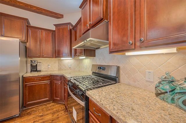 kitchen featuring light stone countertops, stainless steel appliances, under cabinet range hood, backsplash, and wood finished floors